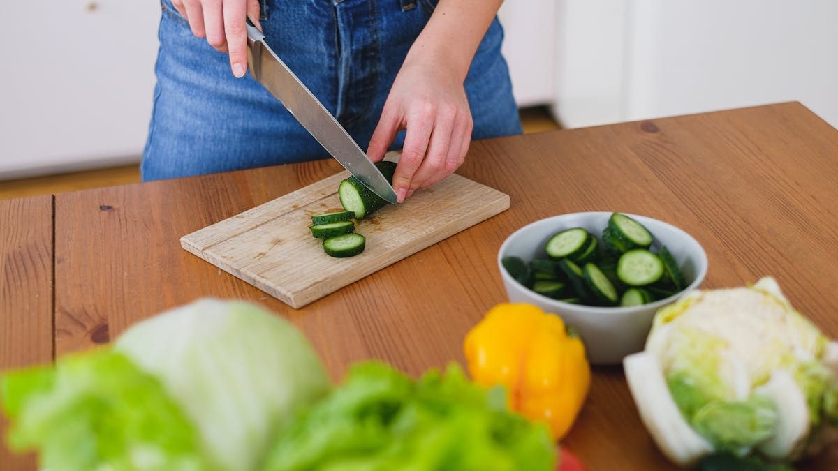 Healthy food preparation with fresh cucumbers and vegetables on a wooden table.
